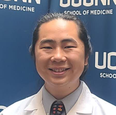 September 2025 Man wearing dress shirt, tie, and lab coat smiling at camera